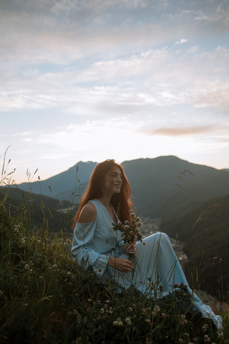 Woman in White Long Sleeve Shirt Sitting on Green Grass Field