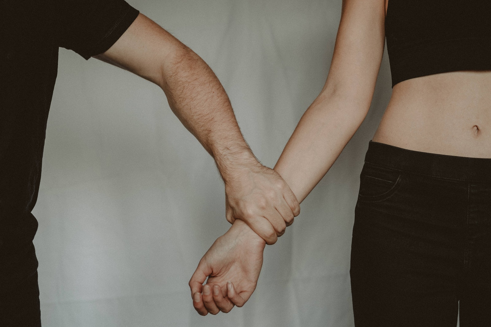 Unrecognizable aggressive man seizing hand of vulnerable helpless woman while standing on white background during domestic violence in light room