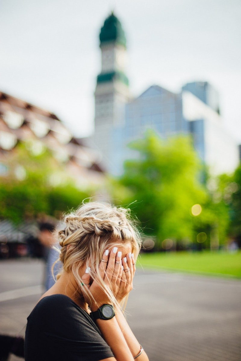 person covering face with hands outdoors