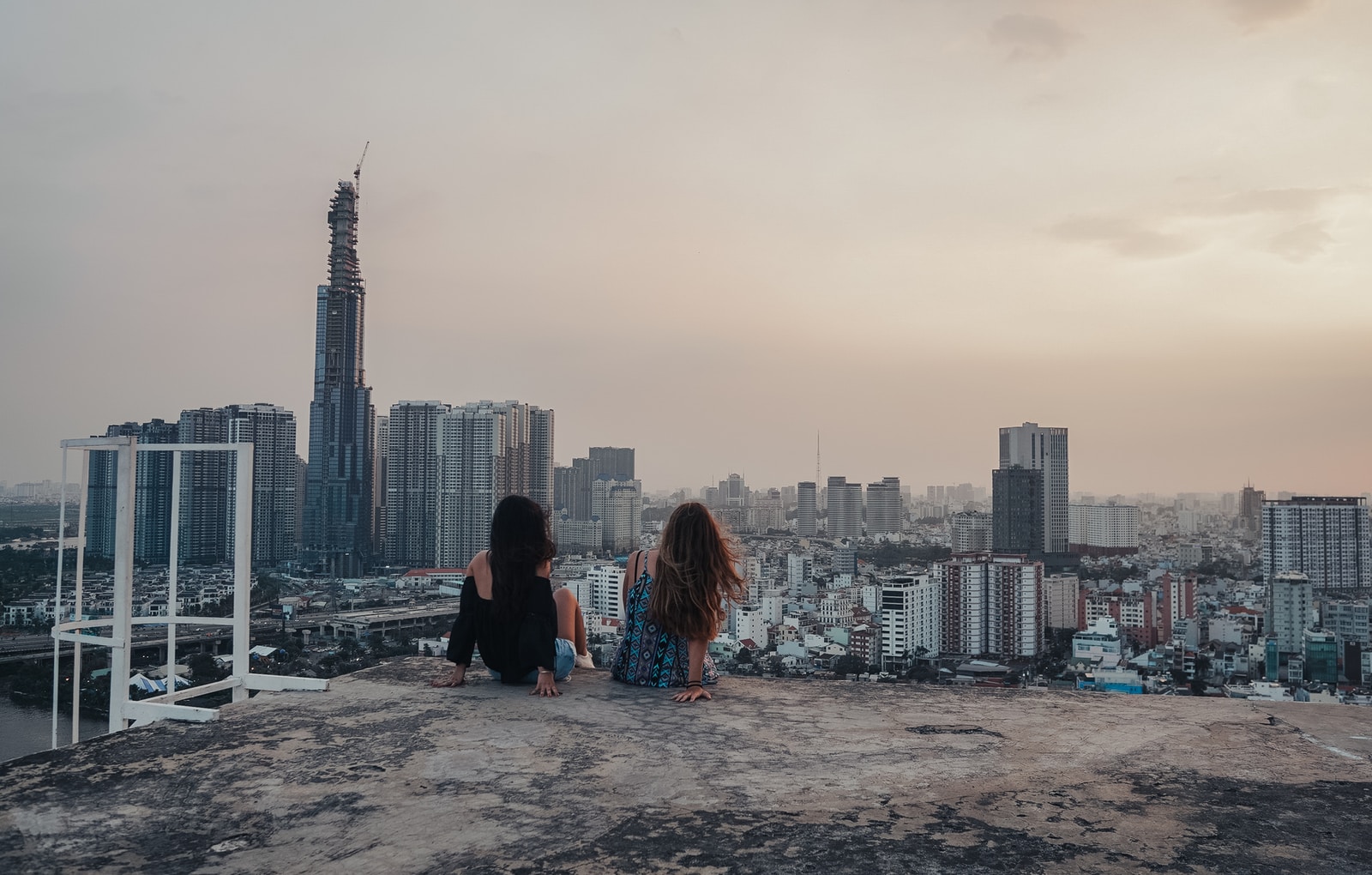 woman in black jacket sitting on gray concrete floor looking at city buildings during daytime