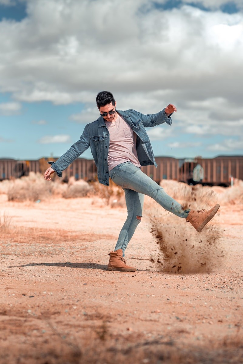 man kicking brown ground under white clouds at daytime